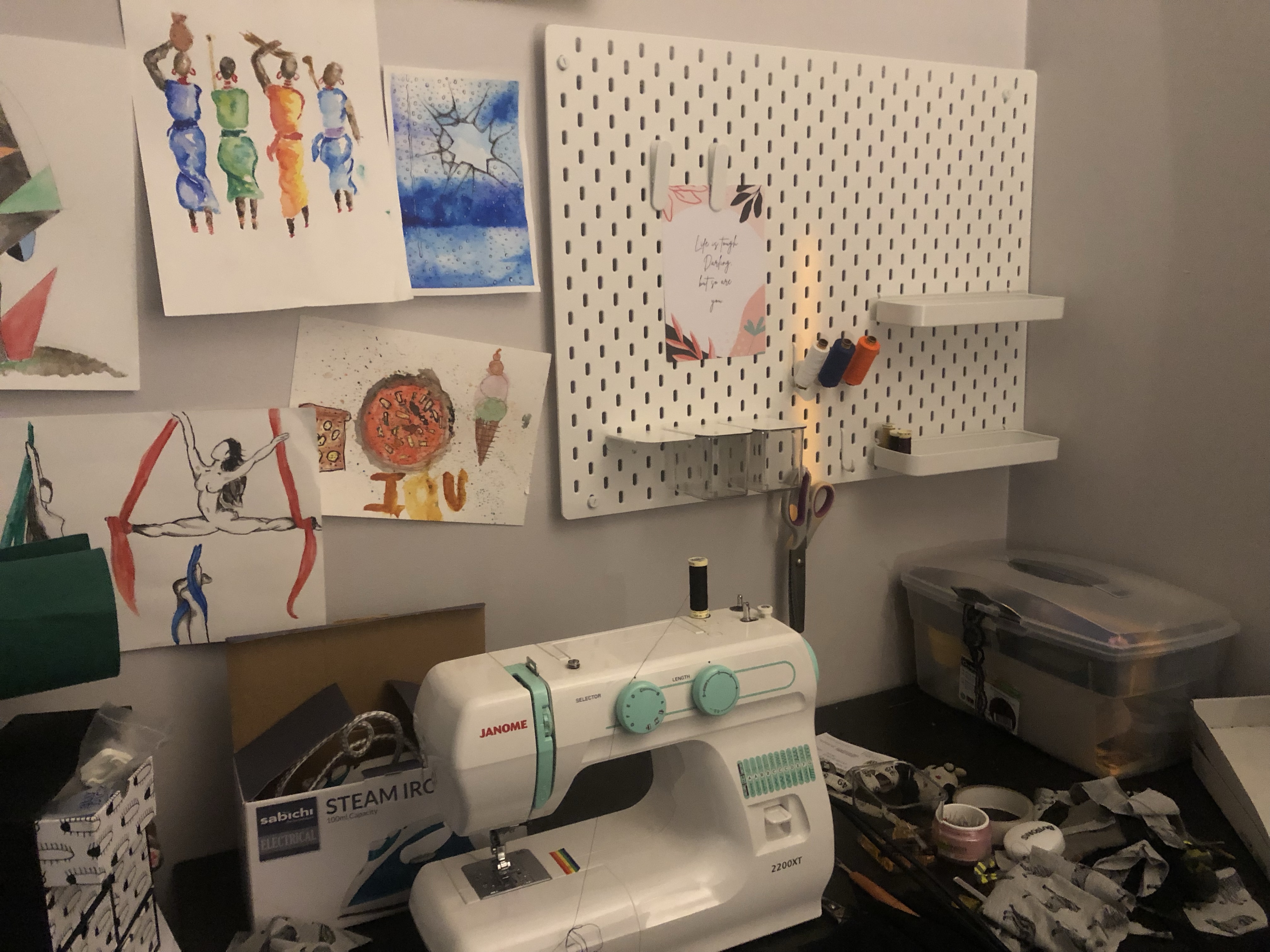 Sewing table with a sewing machine and a pegboard on the wall near some drawings