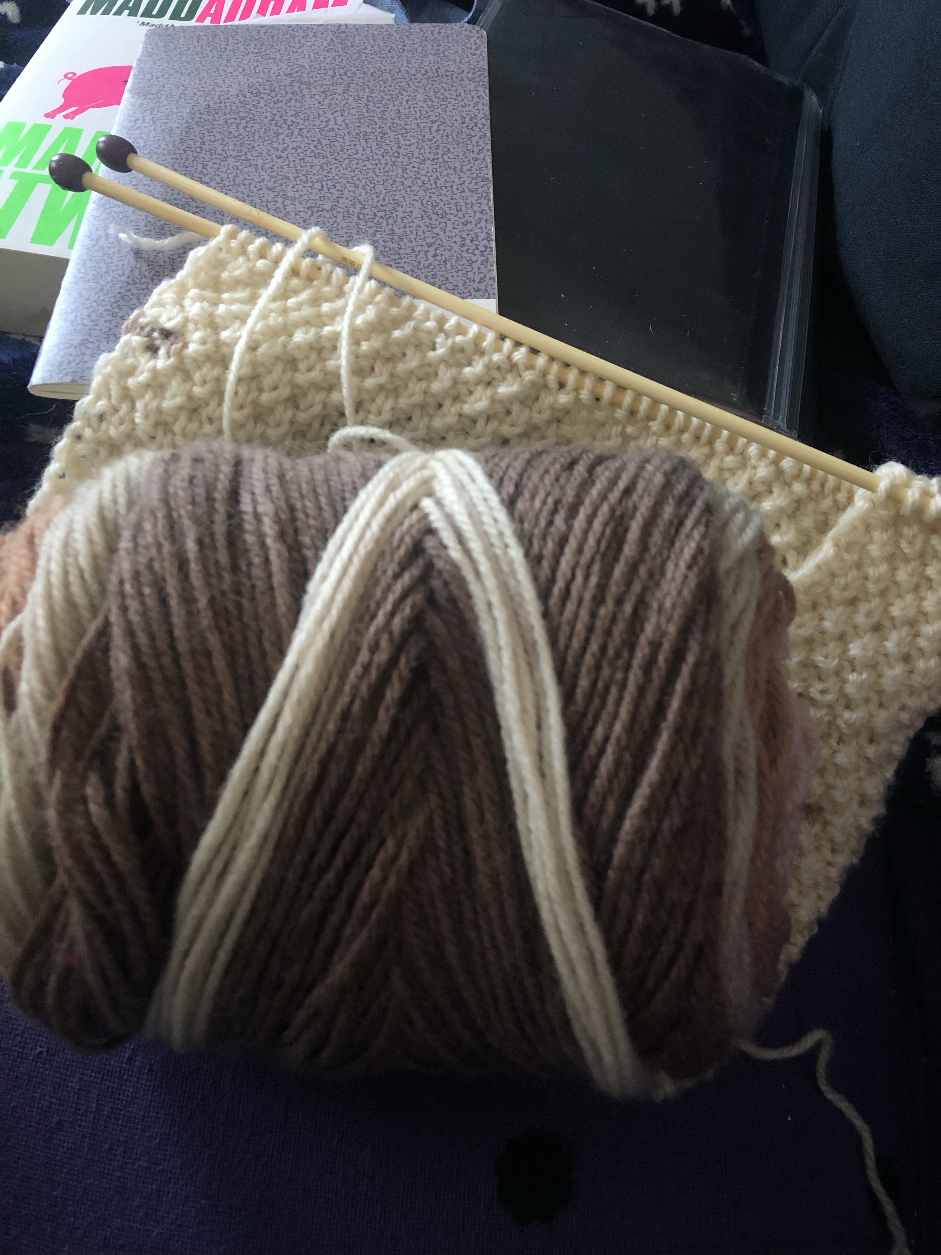 Ball of yarn in beige shades on a knittedh piece with needles