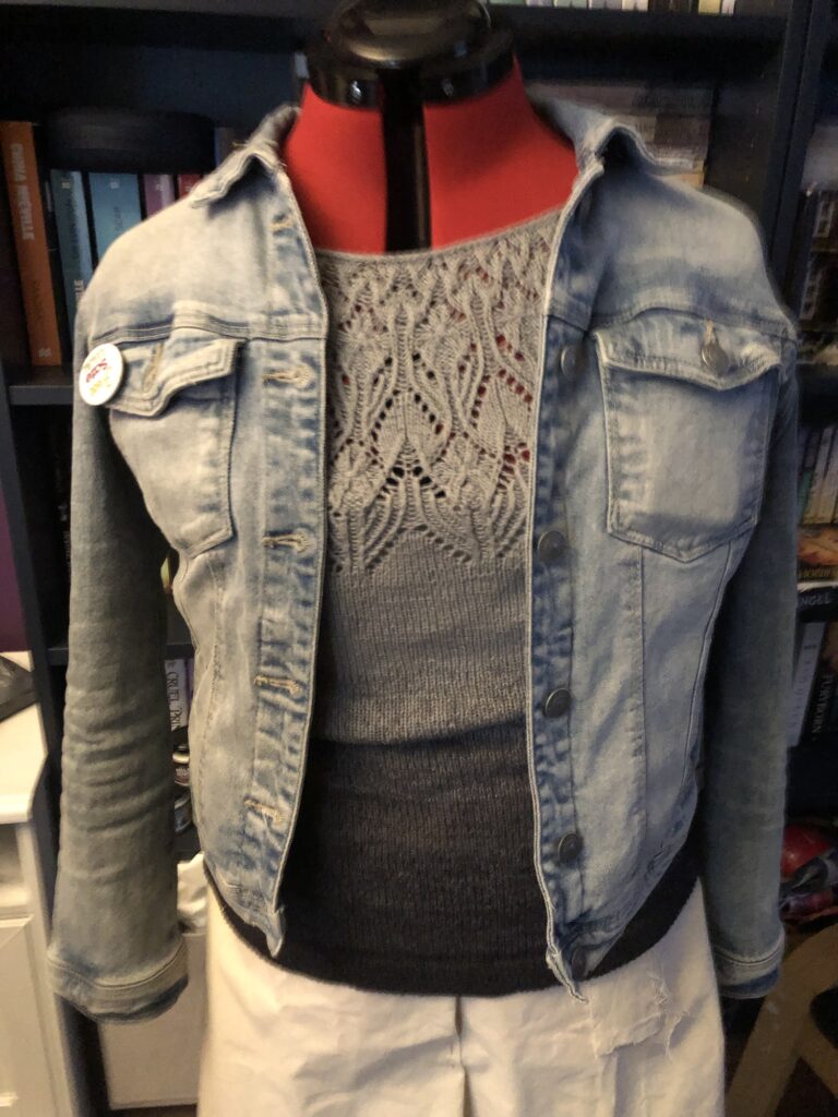 Red dress form wearing a grey top with a lace pattern on the chest under a denim jacket 